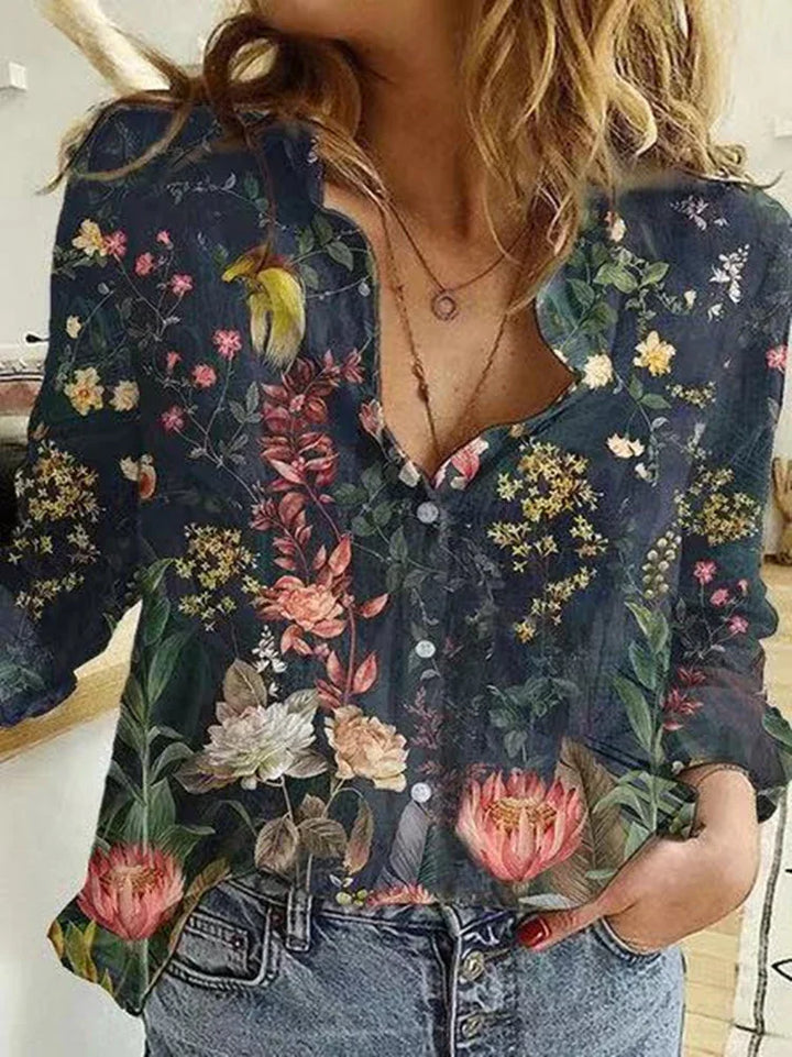 Woman wearing a dark floral button-up blouse with colorful flowers and leaves paired with denim jeans