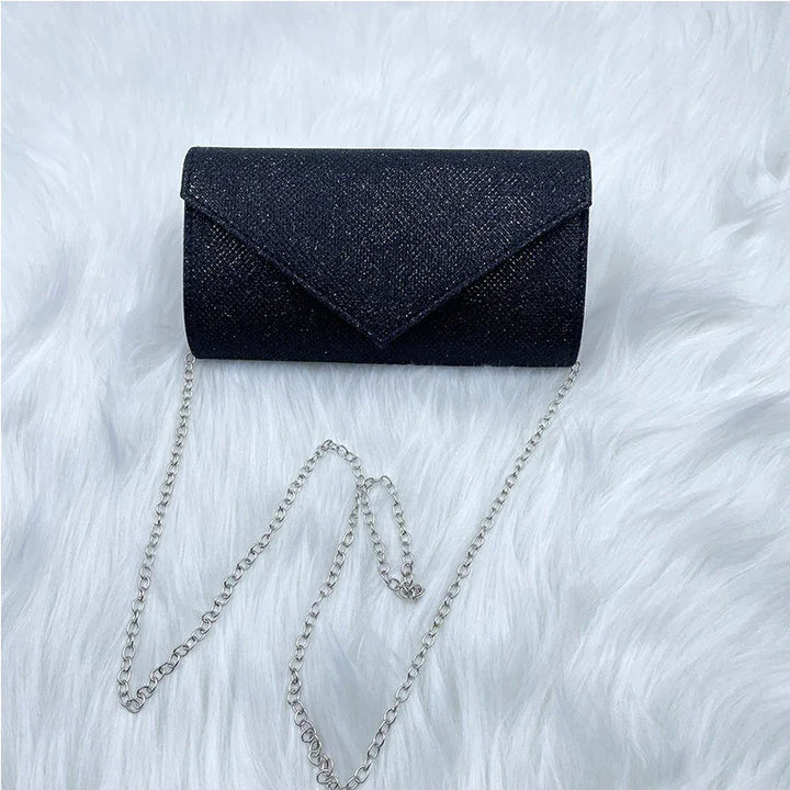 Black glitter clutch purse with silver chain strap on white faux fur background