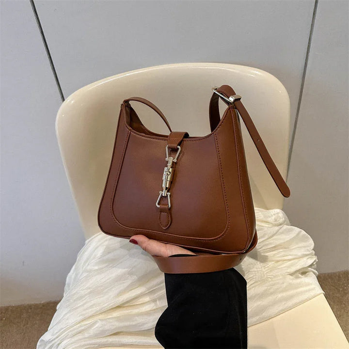 Brown leather handbag with silver clasp held over white chair and fabric background