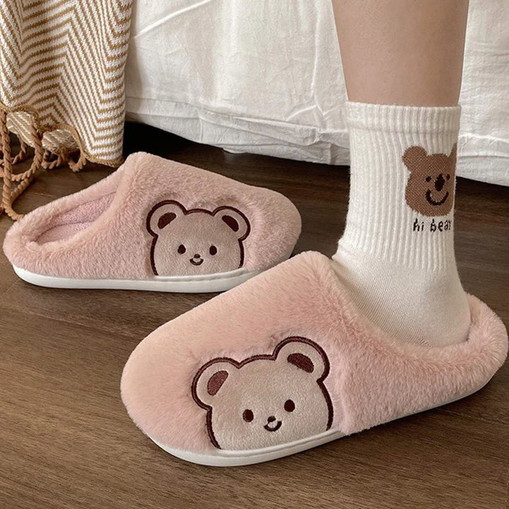 Soft pink fuzzy slippers with smiling bear faces worn with white socks featuring bear design and 'hi bear' text