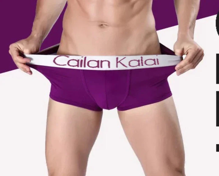 Male model wearing purple Cailan Kalai branded boxer briefs, stretching waistband in studio