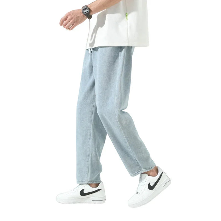 Man wearing light blue denim jeans and white Nike sneakers with black swoosh on white background