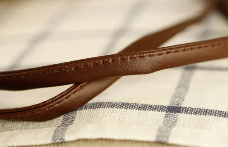 Close-up of brown leather strap with stitching on fabric with black grid pattern