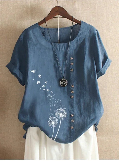 Blue short sleeve blouse with dandelion and bird print, decorative buttons, and paired with white pants