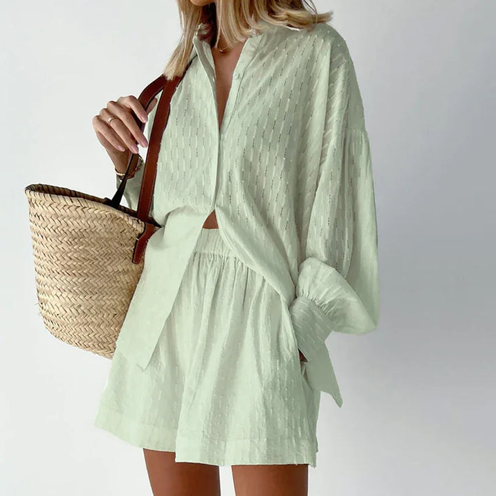 Woman wearing light green textured shirt and shorts outfit holding woven straw tote bag