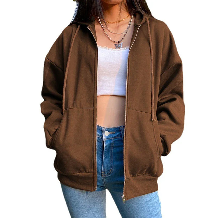 Woman wearing brown zip-up hoodie with pockets, white crop top, and blue jeans