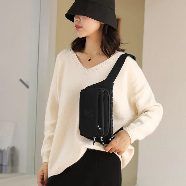 Woman wearing black bucket hat, cream sweater, and black crossbody bag with multiple zippers