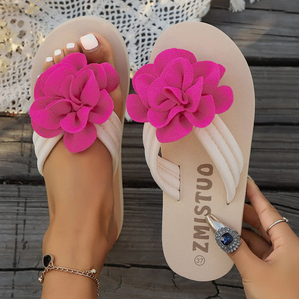 Beige flip-flops with bright pink fabric flower decoration, worn on foot with white pedicure and gold anklet