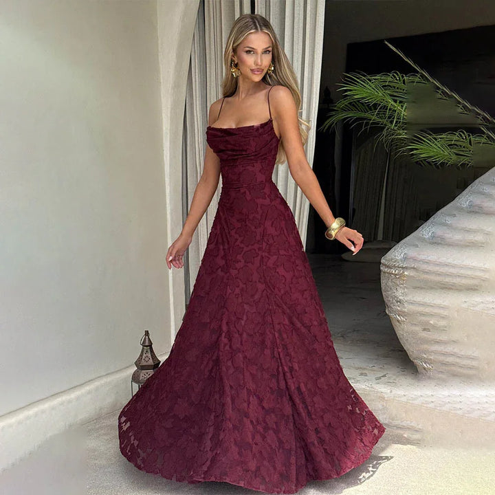 Woman in elegant burgundy floral lace evening gown with spaghetti straps, posing indoors near large planter