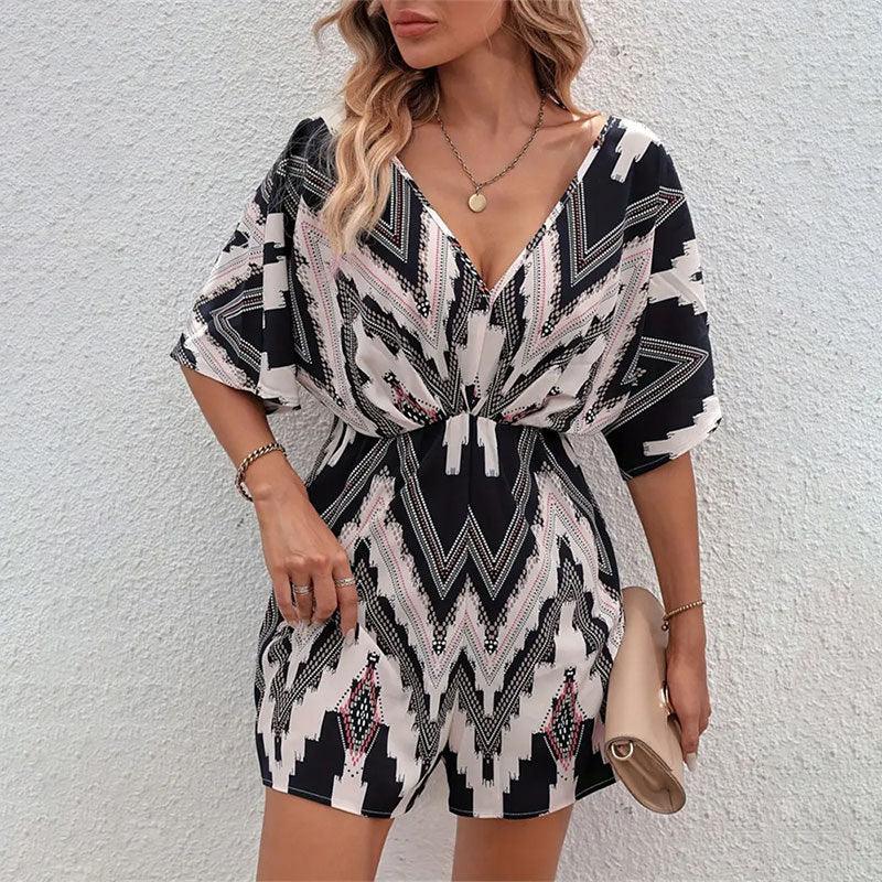 Woman wearing black and beige geometric patterned V-neck romper with short sleeves, holding beige clutch