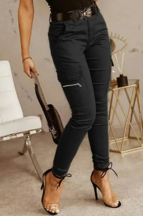 woman wearing black cargo pants with zipper pockets, clear strap high heels, and holding a black handbag in modern indoor setting