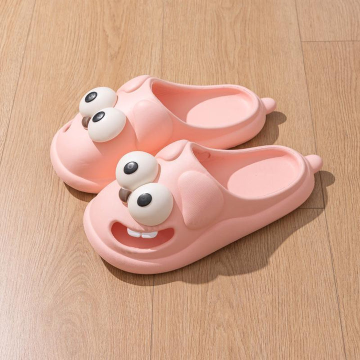 Pink cartoon character slippers with big eyes and teeth on wooden floor