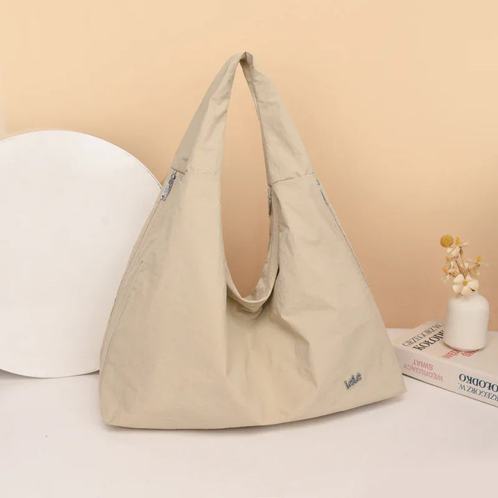 Beige large tote bag with zipper pockets, placed on white surface with books and small vase