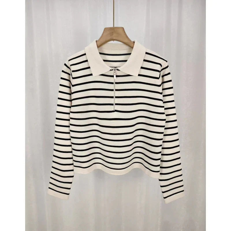 White long-sleeve knit sweater with black horizontal stripes and a zippered collar on a wooden hanger