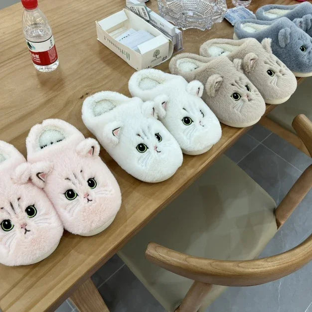 Soft plush cat face slippers in various colors displayed on a wooden table with a chair nearby