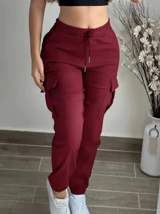 Woman wearing burgundy cargo jogger pants with drawstring waist and white sneakers indoors