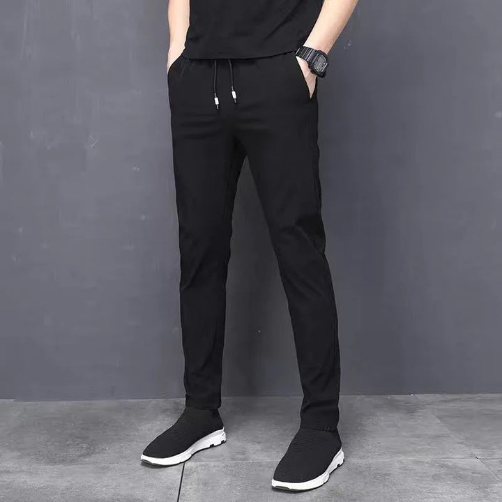 Men's black slim fit jogger pants with drawstring and side pockets, paired with black sneakers