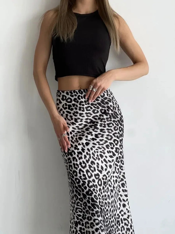 Woman wearing a black crop top and a high-waisted leopard print skirt against a plain wall