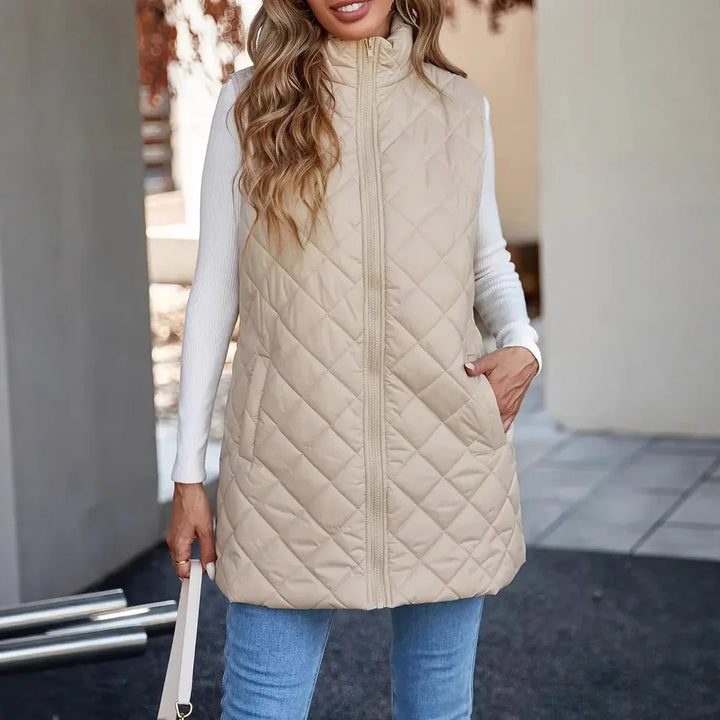 Woman wearing beige quilted sleeveless vest with white long sleeve top and blue jeans
