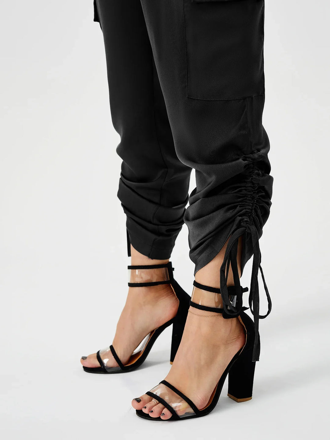 Close-up of feet in black transparent strap high heels paired with black ruched jogger pants