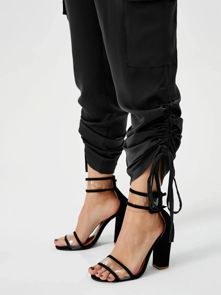 Close-up of feet in black transparent strap high heels paired with black ruched jogger pants