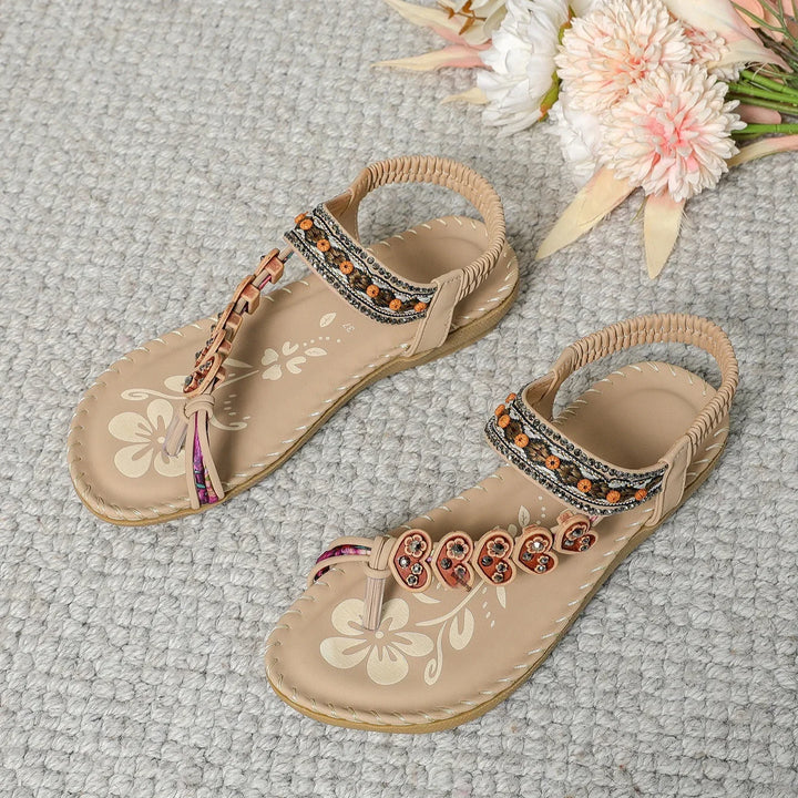 Pair of beige sandals with heart-shaped embellishments and floral print on light gray carpet with flowers