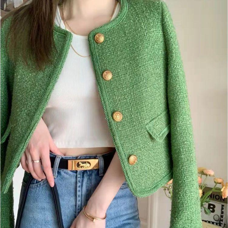 Woman wearing green textured blazer with gold buttons, white crop top, and blue jeans with gold belt buckle