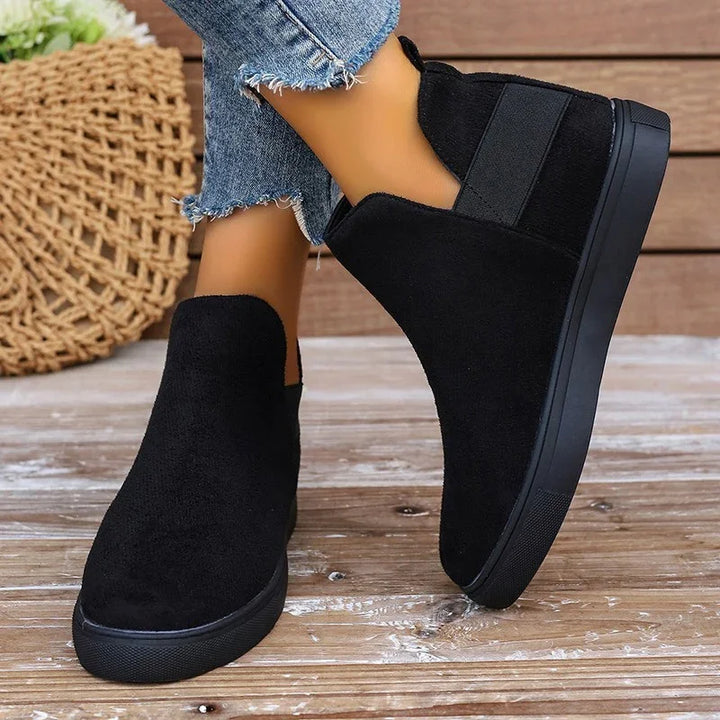 Black suede slip-on ankle boots with elastic side panels worn with frayed hem blue jeans on wooden floor