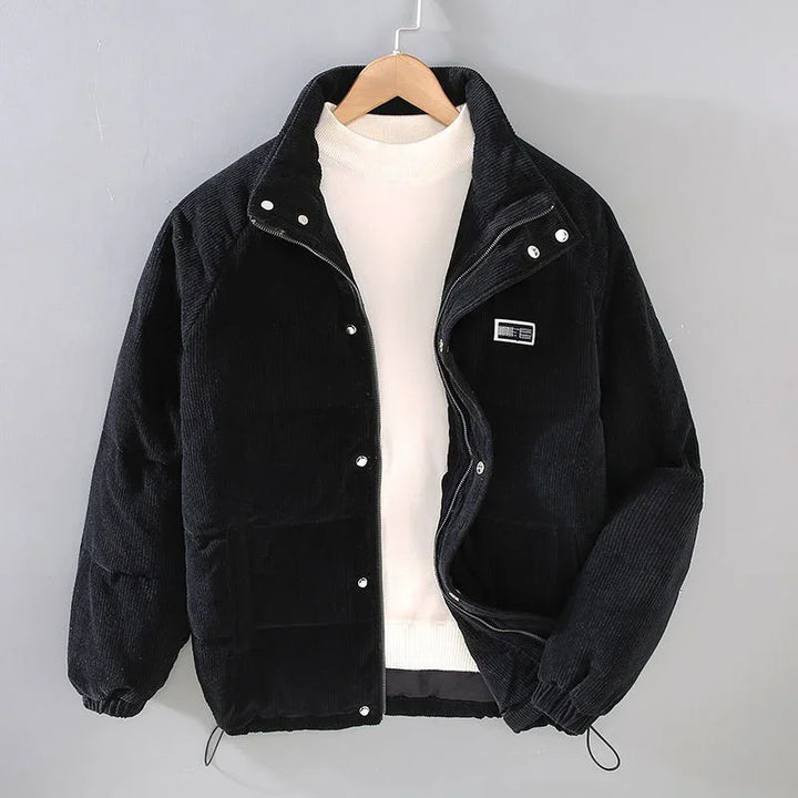 Black corduroy puffer jacket with snap buttons over white turtleneck sweater on wooden hanger