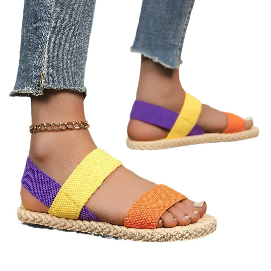 Woman wearing colorful purple, yellow, and orange open-toe flat sandals with braided sole and cropped jeans