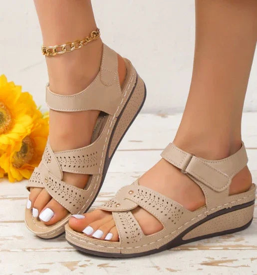 Beige wedge sandals with perforated straps on feet with white toenail polish and gold anklet