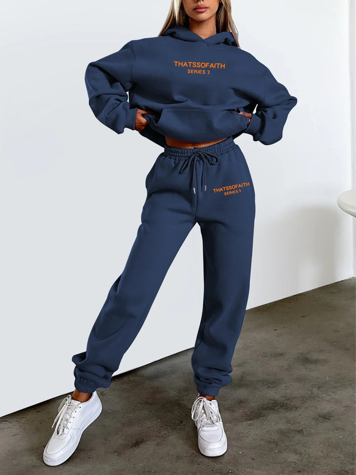 Woman wearing navy blue That'ssofaith Series 2 hoodie and joggers set with white sneakers on concrete floor