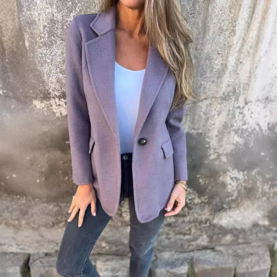 Woman wearing a lilac single-button blazer over a white top and black jeans against textured wall