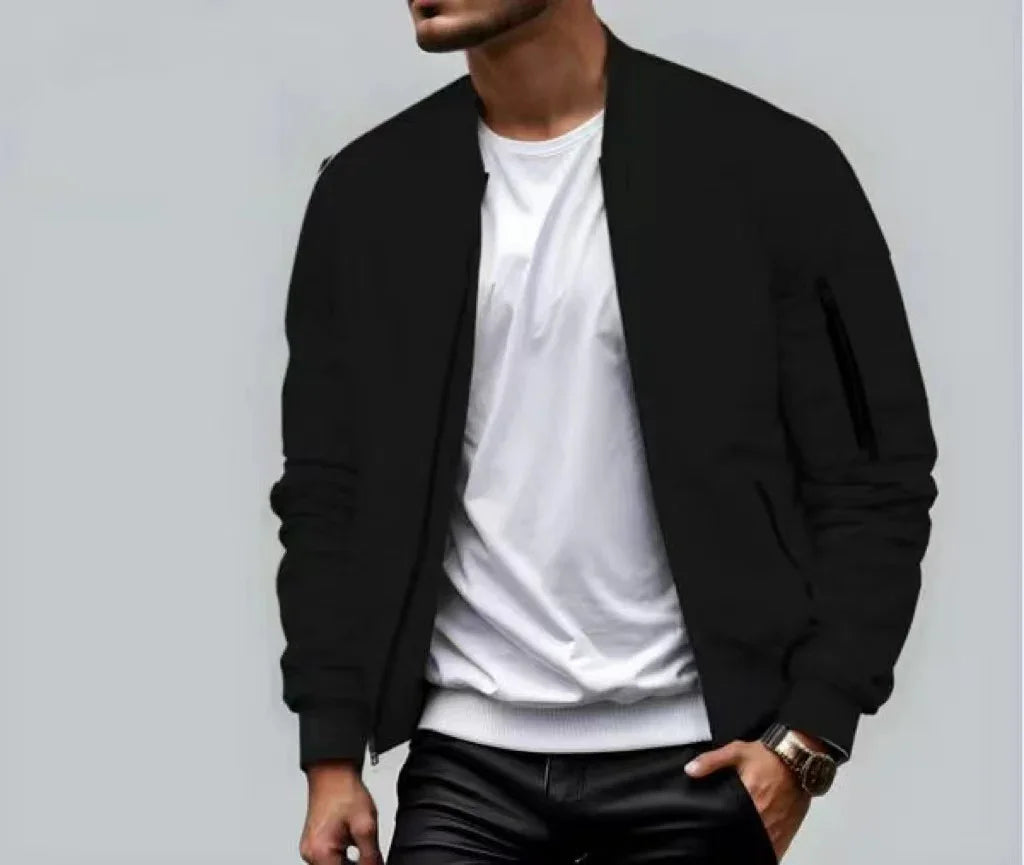 Man wearing black bomber jacket over white t-shirt with black pants against gray background