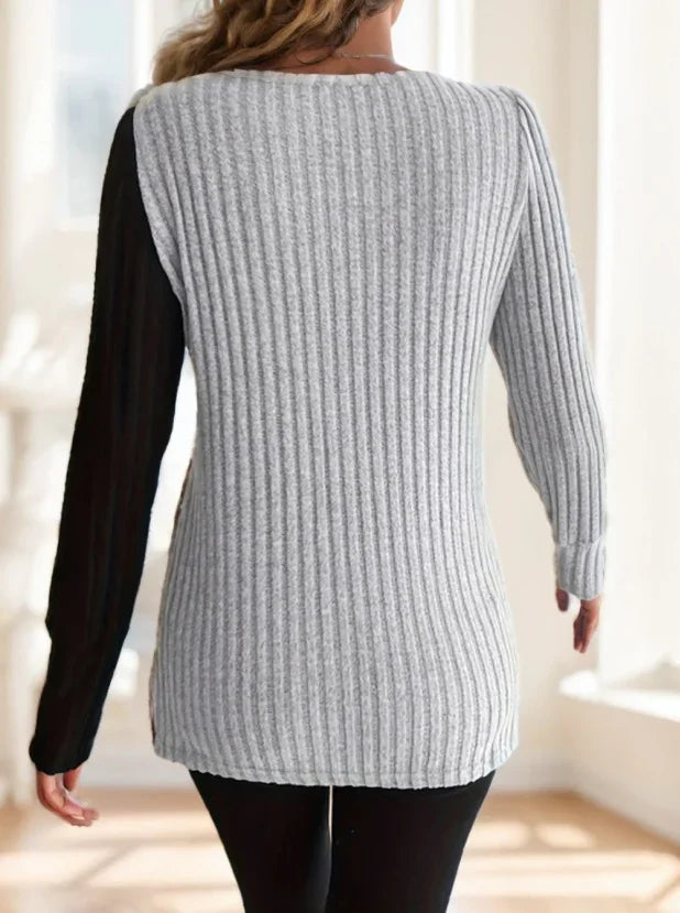 Back view of woman wearing ribbed knit sweater with gray body and black long sleeves indoors