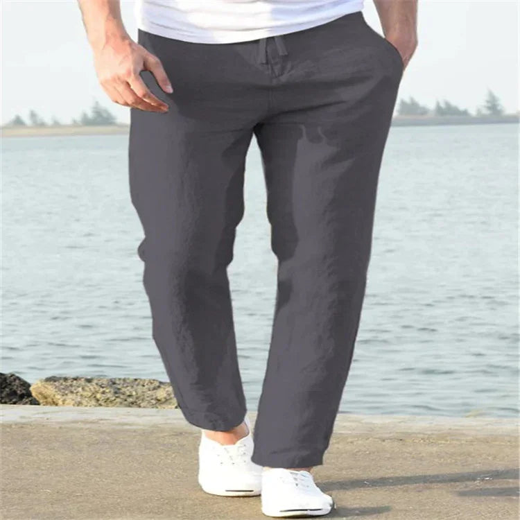 Man wearing dark gray casual pants and white sneakers walking by the waterfront