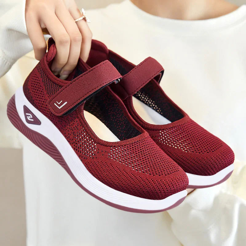 Hand holding lightweight breathable maroon mesh Mary Jane sneakers with white soles