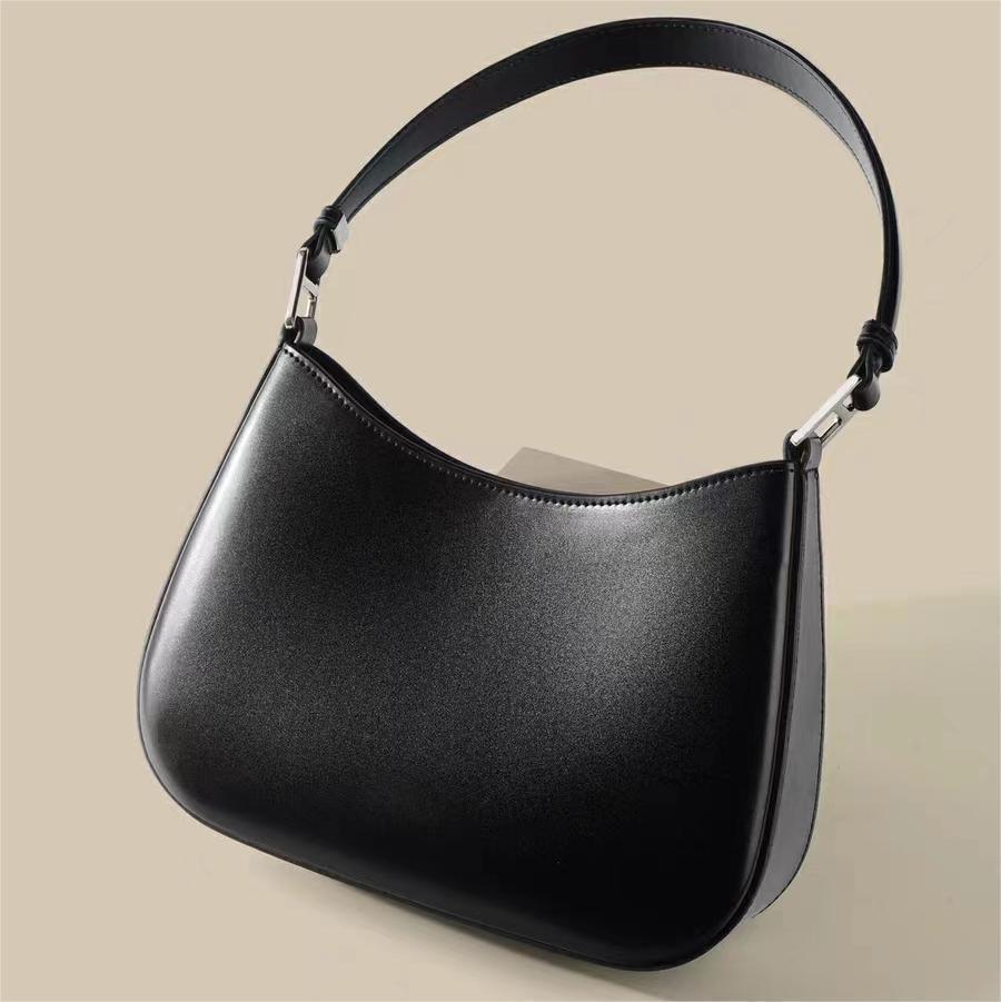 Black leather shoulder handbag with curved top and silver hardware on beige background