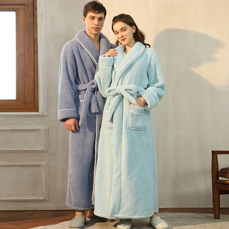 Couple wearing long plush bathrobes in blue and light blue standing indoors near window and chair