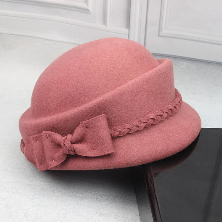 Pink vintage cloche hat with braided band and bow detail on black surface