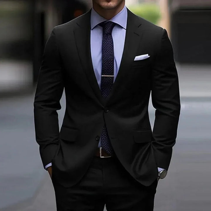 Man wearing black suit, blue shirt, patterned tie, and white pocket square in urban setting