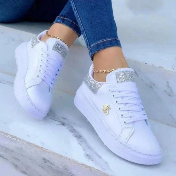 White platform sneakers with silver glitter accents worn with blue jeans on marble stairs