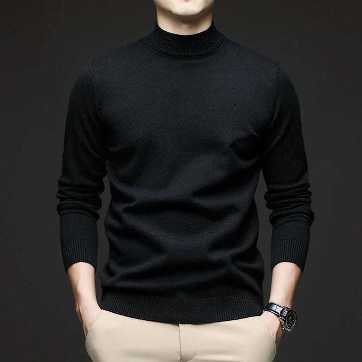 Man wearing black turtleneck sweater with beige pants and wristwatch against dark background