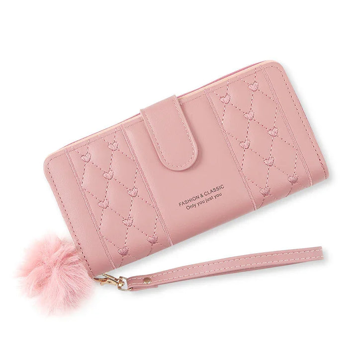 Pink quilted wallet with heart stitching, wrist strap, and fluffy pom pom accessory