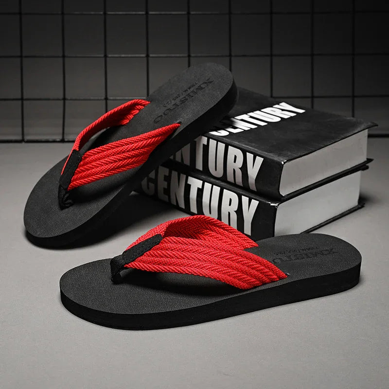 Black flip-flops with bright red braided straps on gray surface near stacked black books titled 'CENTURY'
