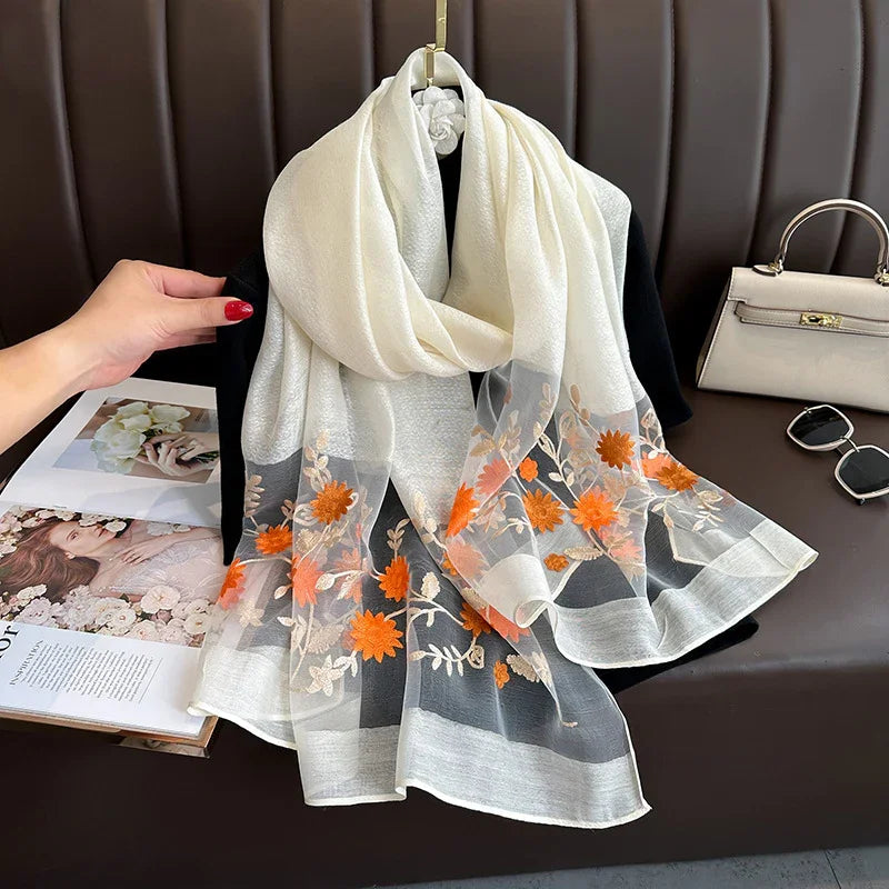 Elegant white chiffon scarf with orange floral embroidery displayed on black fabric with handbag and sunglasses
