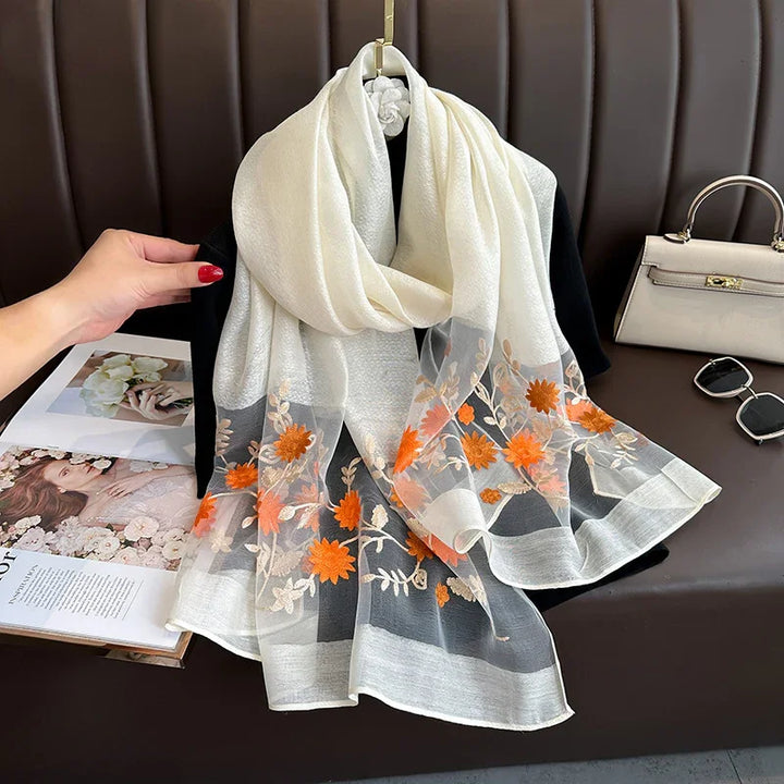 Elegant white chiffon scarf with orange floral embroidery displayed on black fabric with handbag and sunglasses
