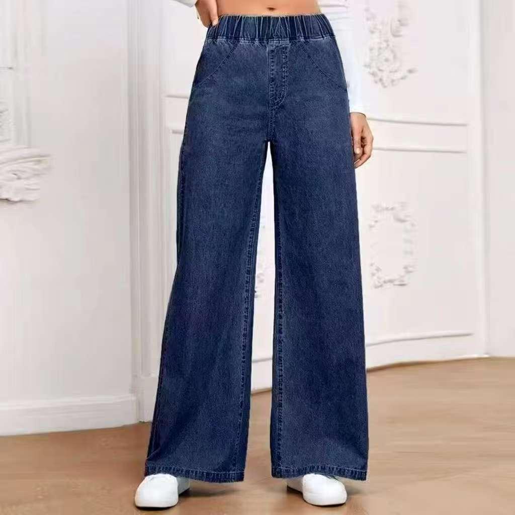 Wide leg dark blue denim jeans with elastic waistband worn with white sneakers indoors
