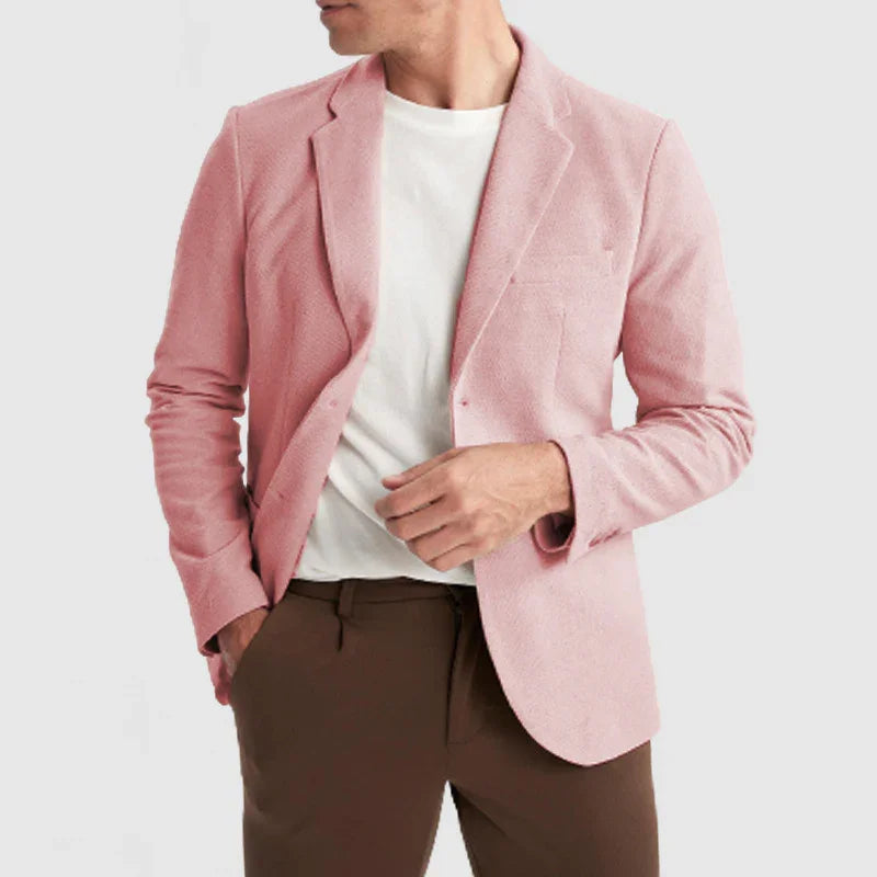 Man wearing light pink blazer with white t-shirt and brown pants against a plain background