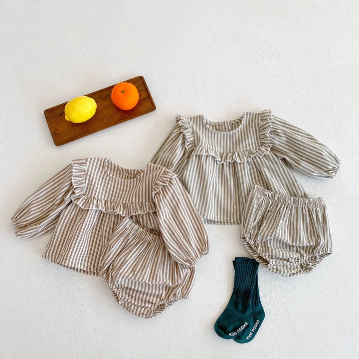 Two striped baby outfits with ruffled collars and bloomers, a wooden tray with lemon and orange, and dark green kids socks